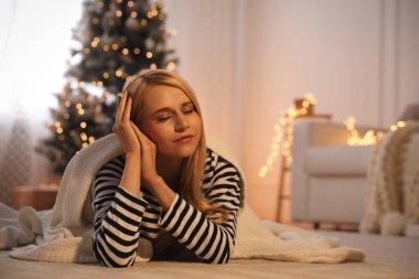 Evdeki halıda battaniyesi olan genç bir kadın, mesaj atmak için yer var. Noel kutlaması