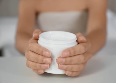 Beyaz masada bir kavanoz nemlendirici kremi olan kadın, yakın plan.