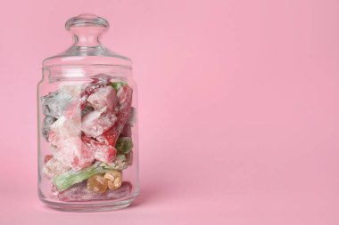 Pembe arka planda cam kavanozda nefis şekerler. Metin için boşluk