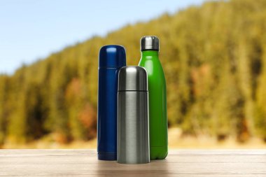 Bulanık dağlara karşı ahşap masada farklı termos şişeleri.