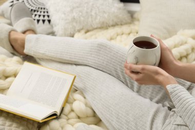 Bir fincan çay ve kitaplı kadın yumuşak ekose üzerinde oturuyor, yakın plan.