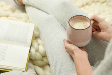 Elinde kahve ve kitapla oturan bir kadın. Yumuşak ekoseli, yakın plan.