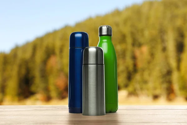Verschiedene Thermosflaschen Auf Holztisch Vor Verschwommenem Berg — Stockfoto