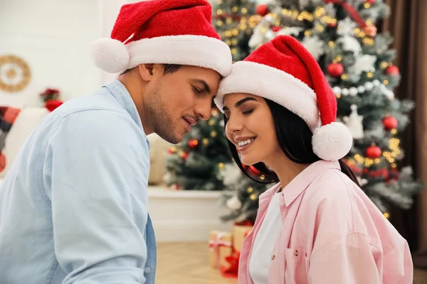 ハッピーカップルでサンタ帽子近くクリスマスツリーで自宅 — ストック写真