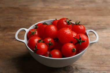 Fresh ripe cherry tomatoes with water drops in colander on wooden table
