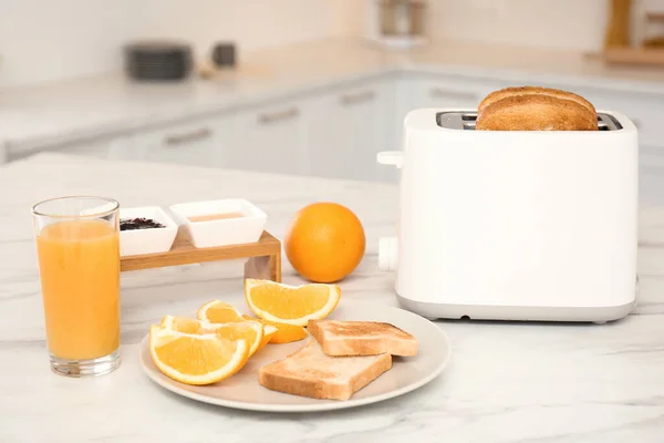 Modern toaster and tasty breakfast on white marble table in kitchen