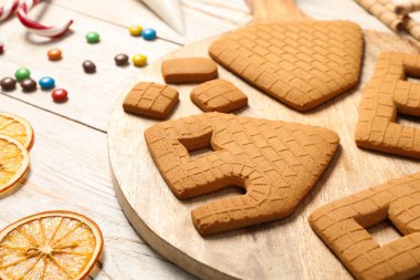 Parts of gingerbread house and ingredients for decoration on white wooden table, closeup