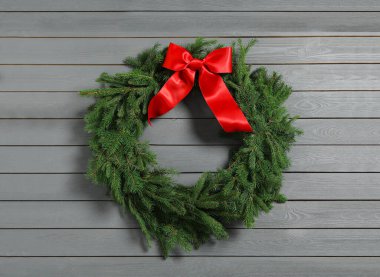 Noel çelengi, gri ahşap arka planda kırmızı fiyonklu köknar dallarından yapılmıştır.