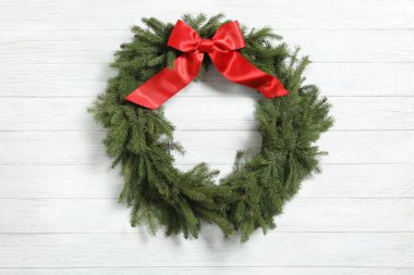 Noel çelengi köknar dallarından yapılmıştır. Beyaz ahşap arka planda kırmızı fiyonk vardır.