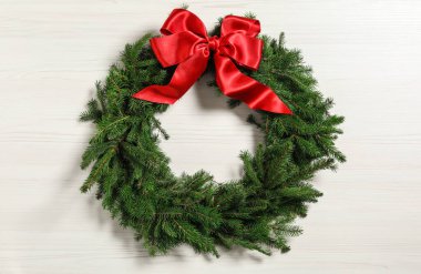 Noel çelengi köknar dallarından yapılmıştır. Beyaz ahşap arka planda kırmızı fiyonk vardır.