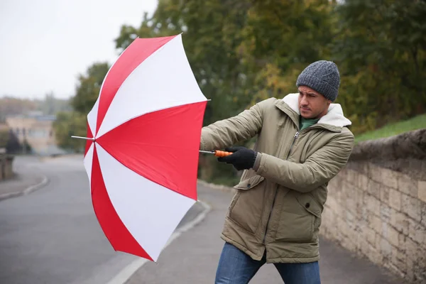 Man with colorful umbrella caught in gust of wind on street