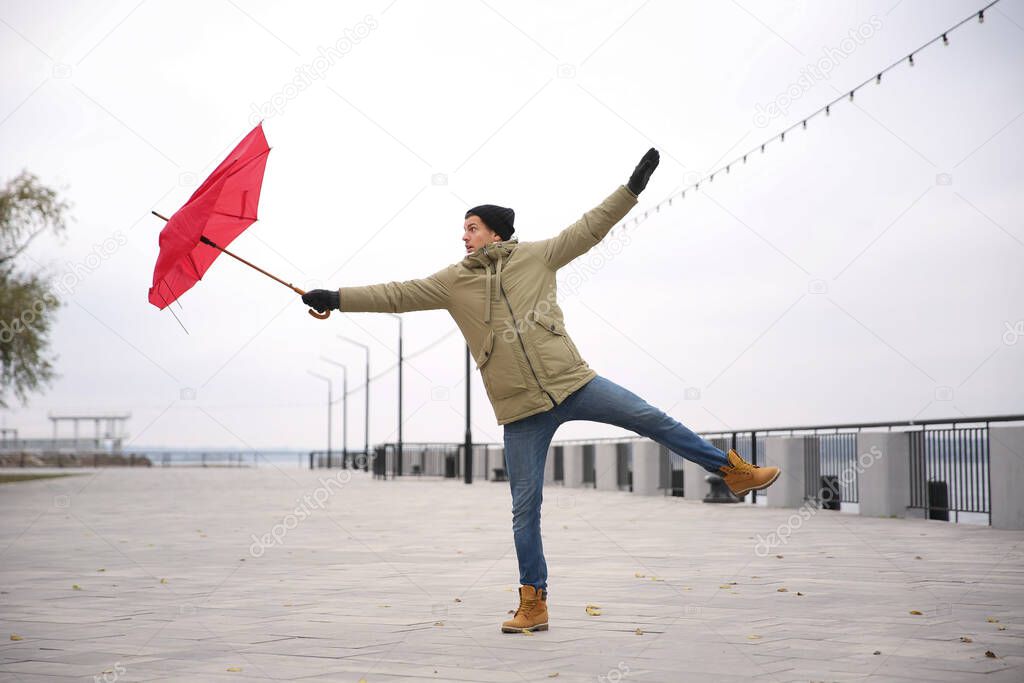 Man with red umbrella caught in gust of wind outdoors