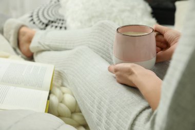 Elinde kahve ve kitapla oturan bir kadın. Yumuşak ekoseli, yakın plan.