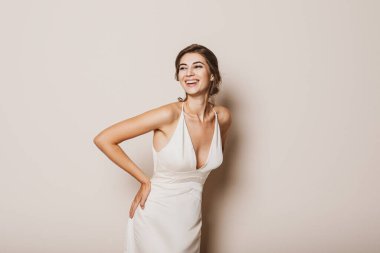 Genç gelin bej arka planda güzel bir gelinlik giyiyor. Metin için boşluk