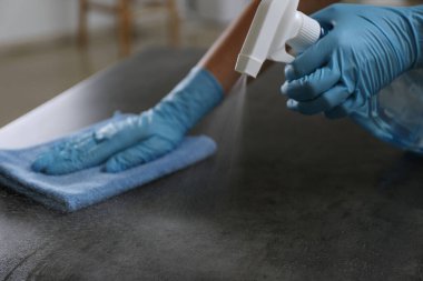 Eldivenli bir kadın, gri taş masayı temizliyor, kapalı alanda bez ve deterjanla, yakın plan.