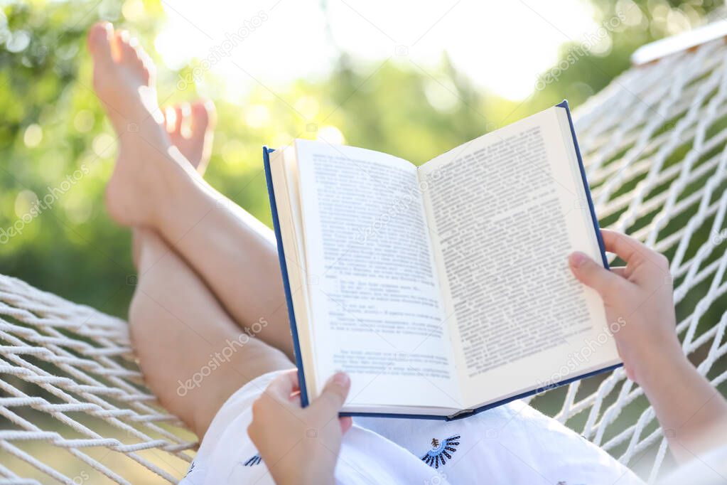 Young woman reading book in comfortable hammock at green garden, closeup