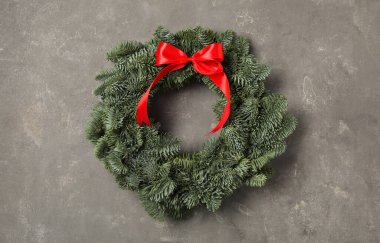 Noel çelengi, köknar ağacı dallarından yapılmıştır, gri arka planda kırmızı kurdele vardır.