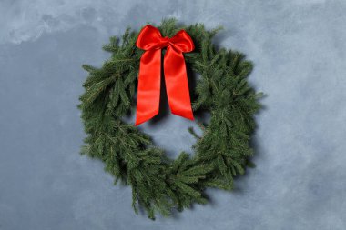 Noel çelengi mavi duvarda kırmızı fiyonklu köknar dallarından yapılmıştır.