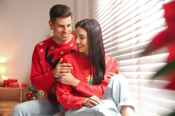 窓の近くの暖かいクリスマスのセーターで幸せなカップル屋内 — ストック写真