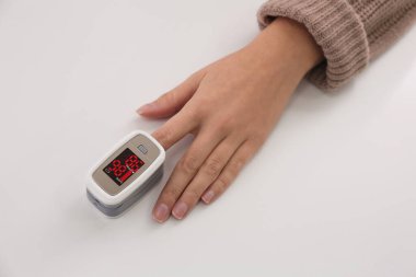 Woman measuring oxygen level with modern fingertip pulse oximeter at white table, top view clipart