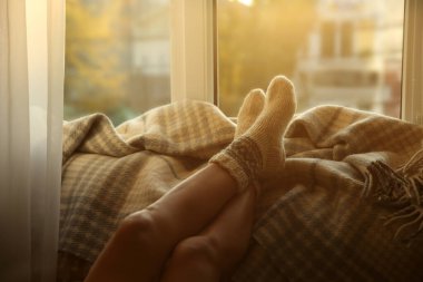 Örgü çoraplı bir kadın. Evinin penceresinin yanında, ekose üzerinde dinleniyor. Kapalı.