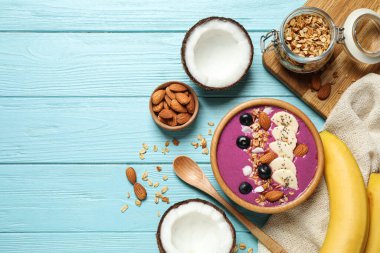 Açık mavi ahşap masada servis edilen granola ve bademli nefis acai smoothie. Metin için boşluk