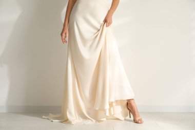 Genç gelin aydınlık duvarın yanında güzel bir gelinlik giyiyor, yakın plan.