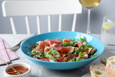 İçerideki gri mermer masada servis edilen olgun incir ve jambonlu salata.