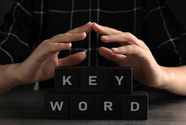 女人在灰色桌子旁展示黑色立方体 用关键词 Keyword — 图库照片