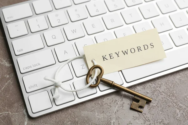 Keyboard, vintage key and tag with word KEYWORDS on grey table, closeup
