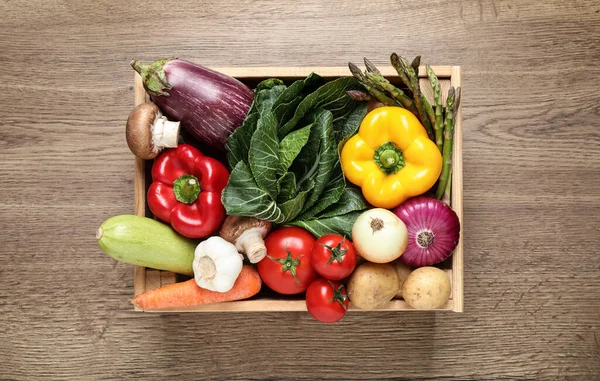 Fresh vegetables in crate on wooden table, top view