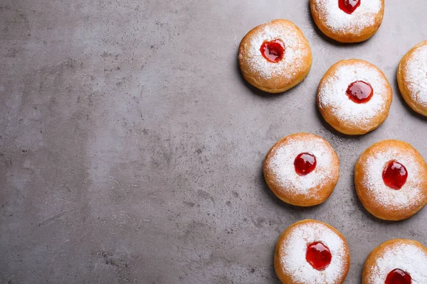 Hanukkah doughnuts with jelly and sugar powder on grey table, flat lay. Space for text
