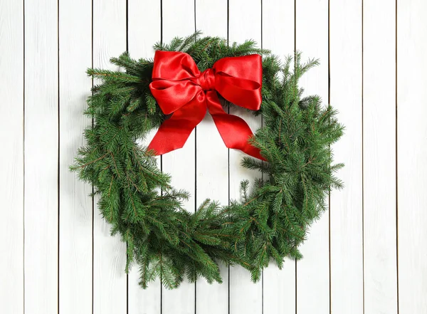 Noel çelengi köknar dallarından yapılmıştır. Beyaz ahşap arka planda kırmızı fiyonk vardır.