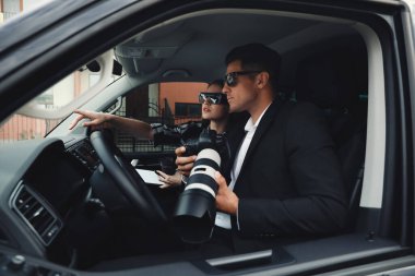 Arabadan gözetleyen modern kameralı özel dedektifler.
