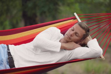 Yeşil bahçede rahat bir hamakta dinlenen adam.