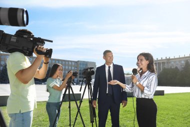 Profesyonel gazeteci ve kameralı operatörler dışarıda röportaj yapıyor.