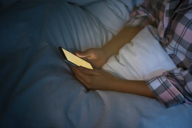 Gece yatakta akıllı telefon kullanan bir kadın, yakın plan. Nomofobi ve uyku bozukluğu sorunu