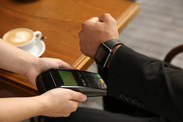 Man making payment with smart watch in cafe, closeup