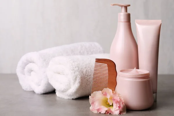 Different hair products, rolled towels and wooden comb on grey table