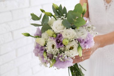 Gelin, Eustoma çiçekleriyle birlikte tuğla duvarın yanında güzel bir buket tutuyor.