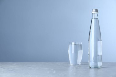 Açık mavi arkaplan üzerinde su olan cam ve şişe, metin için boşluk