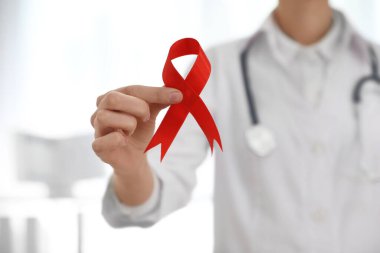 Arka planda kırmızı kurdele tutan doktor, yakın plan. AIDS Farkındalık Ayı