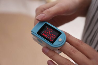 Woman measuring oxygen level with modern fingertip pulse oximeter indoors, closeup clipart