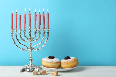 Gümüş menorah, dreidels with He, Pe, Nun, Gimel letters and sufganiyot on white table, space for text. Hanuka sembolleri