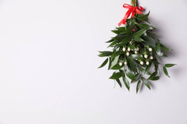 Beyaz duvarda asılı kırmızı kurdeleli ökseotu sürüsü, mesaj için yer var. Geleneksel Noel dekorasyonu