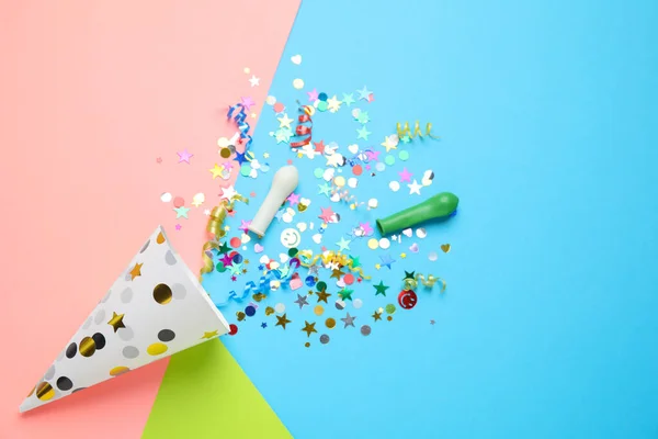 Bright confetti with party cracker on color background, flat lay