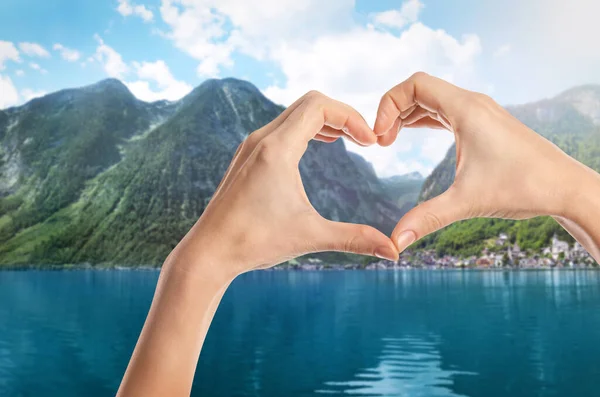 Woman making heart with hands near lake and mountains on sunny day, closeup