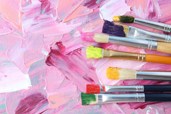 Set of different brushes on abstract colorful paint, flat lay