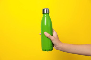 Sarı arka planda modern yeşil termos tutan kadın, yakın plan.