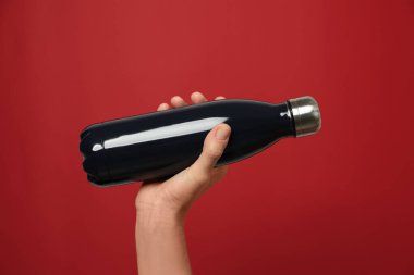 Kırmızı arka planda modern siyah termos tutan kadın, yakın plan.